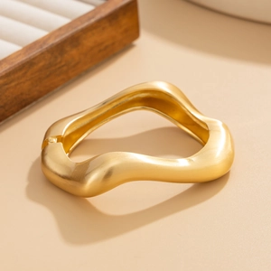 Detail view of gold irregular wavy bracelet with matte brushed texture and hinge closure