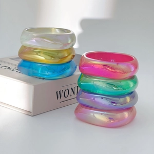 Bracciali geometrici in resina dai colori perlati cangianti impilati su dei libri