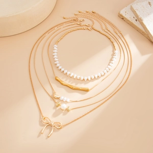 Golden 4-layer necklace set featuring pearls, bow pendant, and heart charms on warm background
