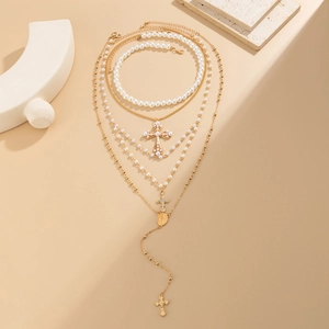 Layered gold cross pendant necklace with faux pearls on warm sand background