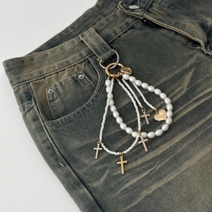 Close-up of hip-hop cross and heart charms on multilayered pearl and metal belt chain