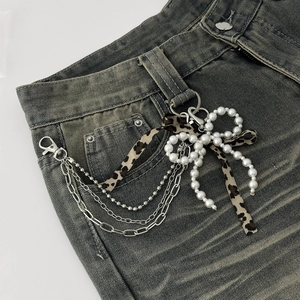 Detail of multi-layer metal chain with pearl bow and leopard ribbon on denim