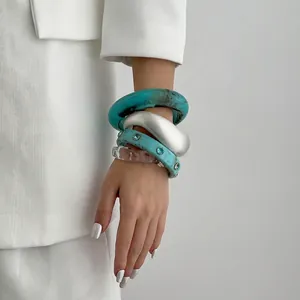 Stacked set of blue marble resin and crystal-studded silver bangles on a white blazer cuff