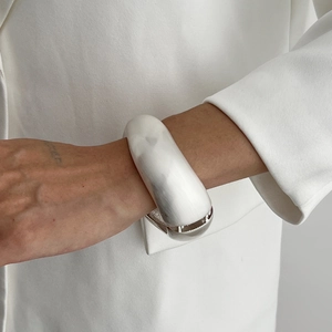 Close-up of a minimalist silver wide metal bangle on a wrist with white blazer