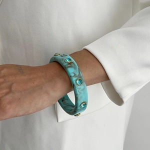 Detail of turquoise marble resin bangle with blue crystal studs on a white blazer