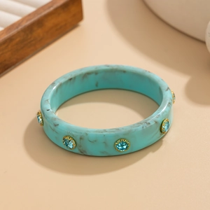 Detailed view of light blue marble resin bangle featuring inlaid blue gems in gold settings