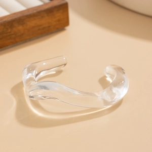 Detail view of transparent acrylic irregular wavy bangle on a neutral beige background