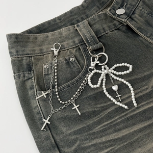 Detail of silver layered waist chain with pearl bow and crosses on denim jeans