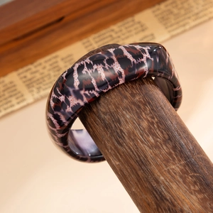 Macro detail of glossy leopard print resin bangle on a rustic wooden display stand