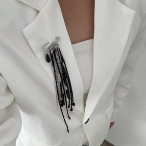 Détail d'une broche à longs glands perlés avec pendentif noir sur revers blanc