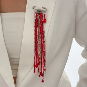 Vue détaillée d'une broche à glands perlés rouges et chaîne argentée sur blazer blanc