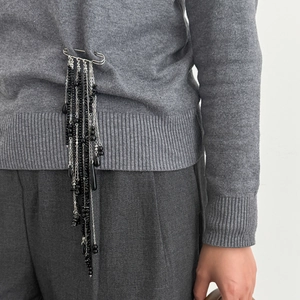 Detail of silver safety pin brooch with black beads and chain tassels on grey sweater