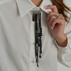 Détail d'une broche vintage perlée noire avec des chaînes argentées sur un col de chemise