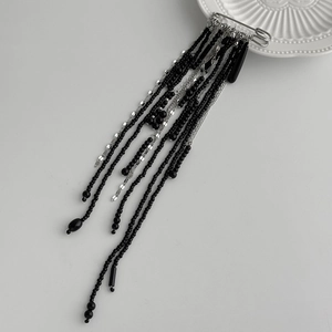 Detail of silver safety pin brooch with hanging black crystal beads and metal tassels