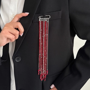Detailed view of silver safety pin brooch with red beads and long tassel chains