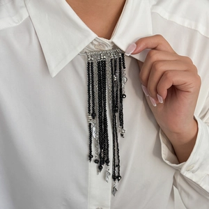 Détail de la broche à franges perlées avec chaînes argentées sur un col de chemise