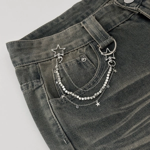Detail of layered silver chain accessory with stars and moon on denim jeans