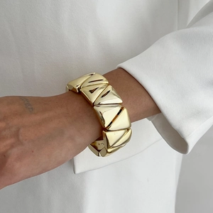 Détail d'un bracelet manchette doré large au design géométrique irrégulier et moderne