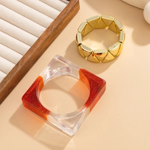 Détail du bracelet géométrique en métal et du jonc en résine orange sur présentoir