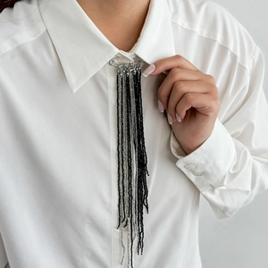 Silver safety pin brooch with long black and white beaded tassels on white shirt collar