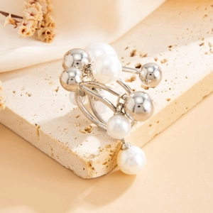 Close-up of a multi-layer silver ring with faux pearls on a beige stone surface