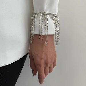 Dettaglio del bracciale a catena con nappe argentate e perle su una manica bianca