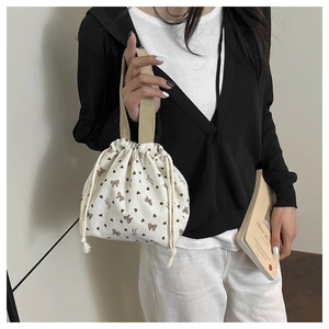 Detail of beige corduroy drawstring bucket bag with brown bow patterns and fabric handles