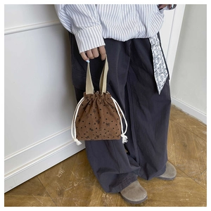 Detail of a brown corduroy drawstring handbag featuring cute black bow floral patterns