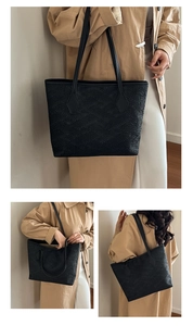 Detailed view of black tote bag with woven texture and slender leather shoulder straps