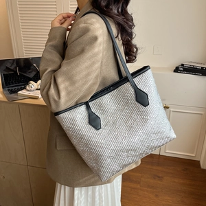 Large silver tote bag with metallic texture and black leather straps on a female model