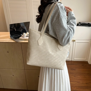 Close-up of beige tote bag featuring vertical ribbed texture and slim leather strap