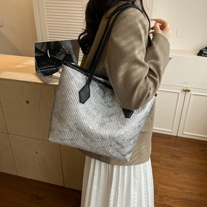 Detail of silver metallic quilted tote bag with black leather shoulder straps on model
