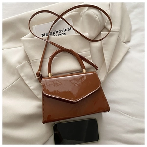 Detail of caramel patent leather bag with triangular flap and gold metal hardware