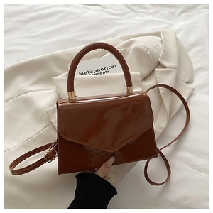 Detail of brown patent leather handbag with gold hardware and curved handle on fabric