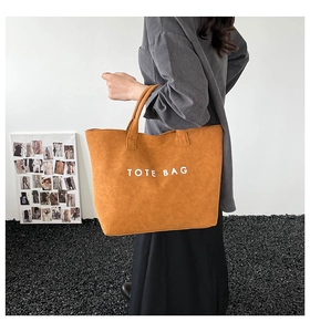 Detail view of large camel suede tote bag with TOTE BAG lettering held by a model