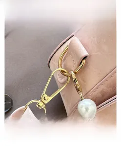 Detail of pink shell bag with golden snap hook and white pearl shoulder strap