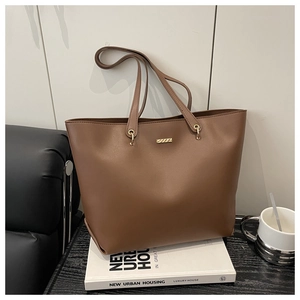 Detail of a brown PU leather tote bag with gold metal buckle on white books background