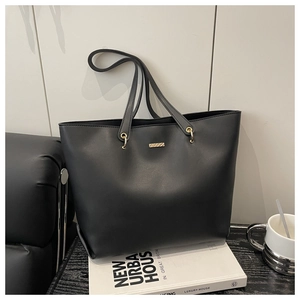 Detail of a large black leather tote bag with elegant gold hardware on an urban book