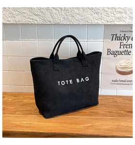 Close-up of black tote bag with white TOTE BAG lettering on matte textured fabric