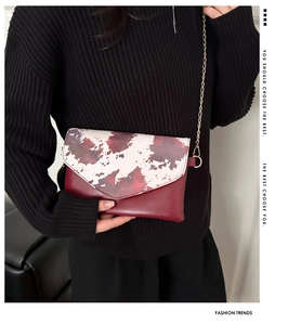 Detail of red crossbody chain bag with cow print flap on a black knit sweater