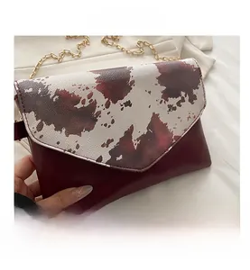 Close-up of cow print patterned flap and golden chain strap on a brown shoulder bag