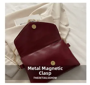 Detail of burgundy envelope bag featuring a gold chain strap and magnetic snap closure