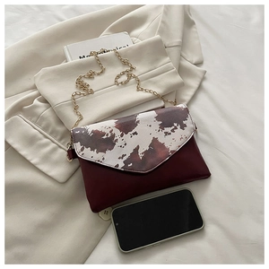 Detail of crossbody envelope bag with cow print flap and wine red leather texture