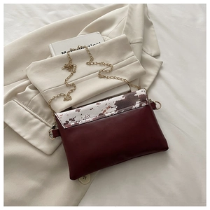 Detail of burgundy crossbody bag featuring cow print flap and gold metal chain strap