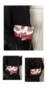 Detail of burgundy envelope bag with marble pattern flap and gold chain strap