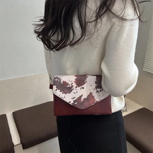 Fashionable cow print crossbody bag with burgundy leather and golden chain strap