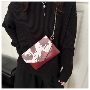 Detail of red crossbody bag with cow print flap and golden chain strap on model
