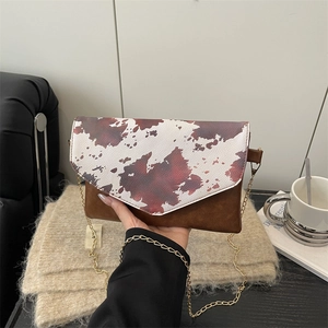 Close-up of envelope crossbody bag featuring brown suede and cow print pattern with gold chain