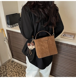 Detail einer braunen Wildleder-Beuteltasche mit Plüschbären-Anhänger an einem Model