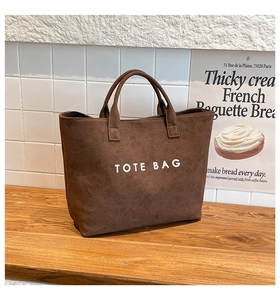 Detail view of brown suede tote bag featuring bold white text in a minimalist French setting